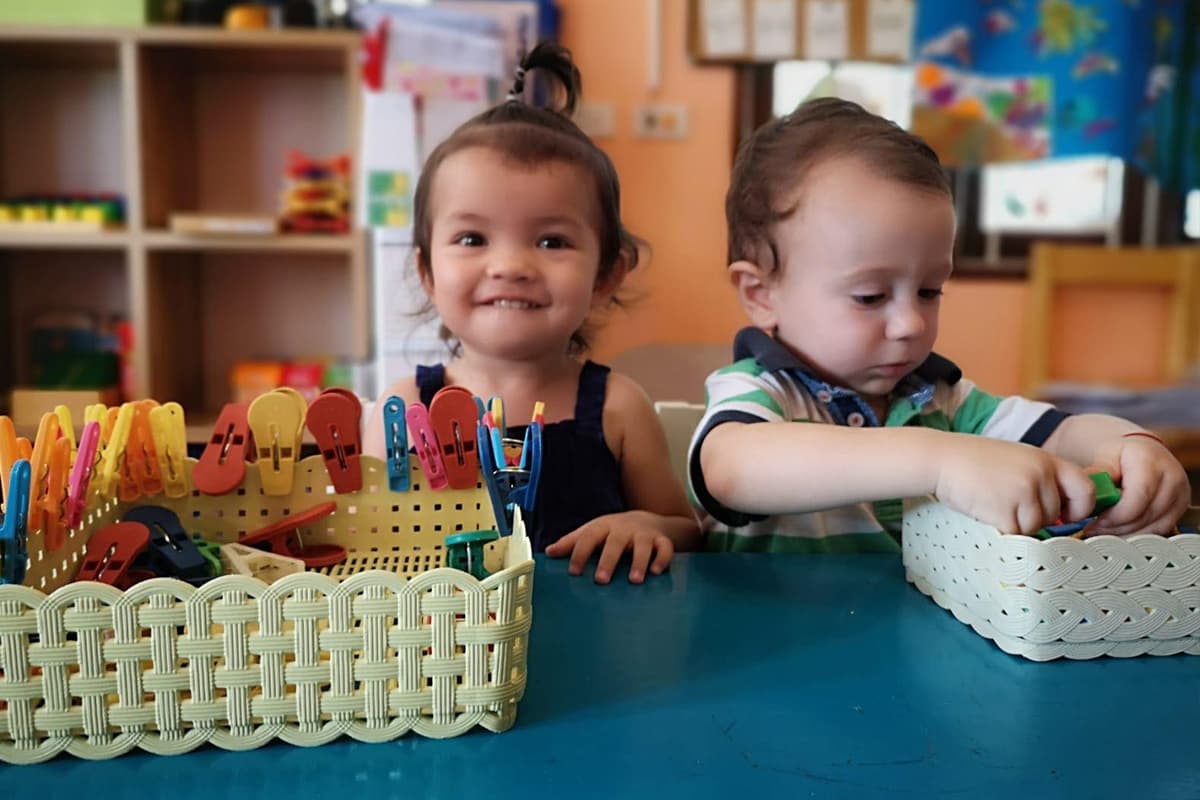 Two toddlers sorting coloured clothes pegs into baskets