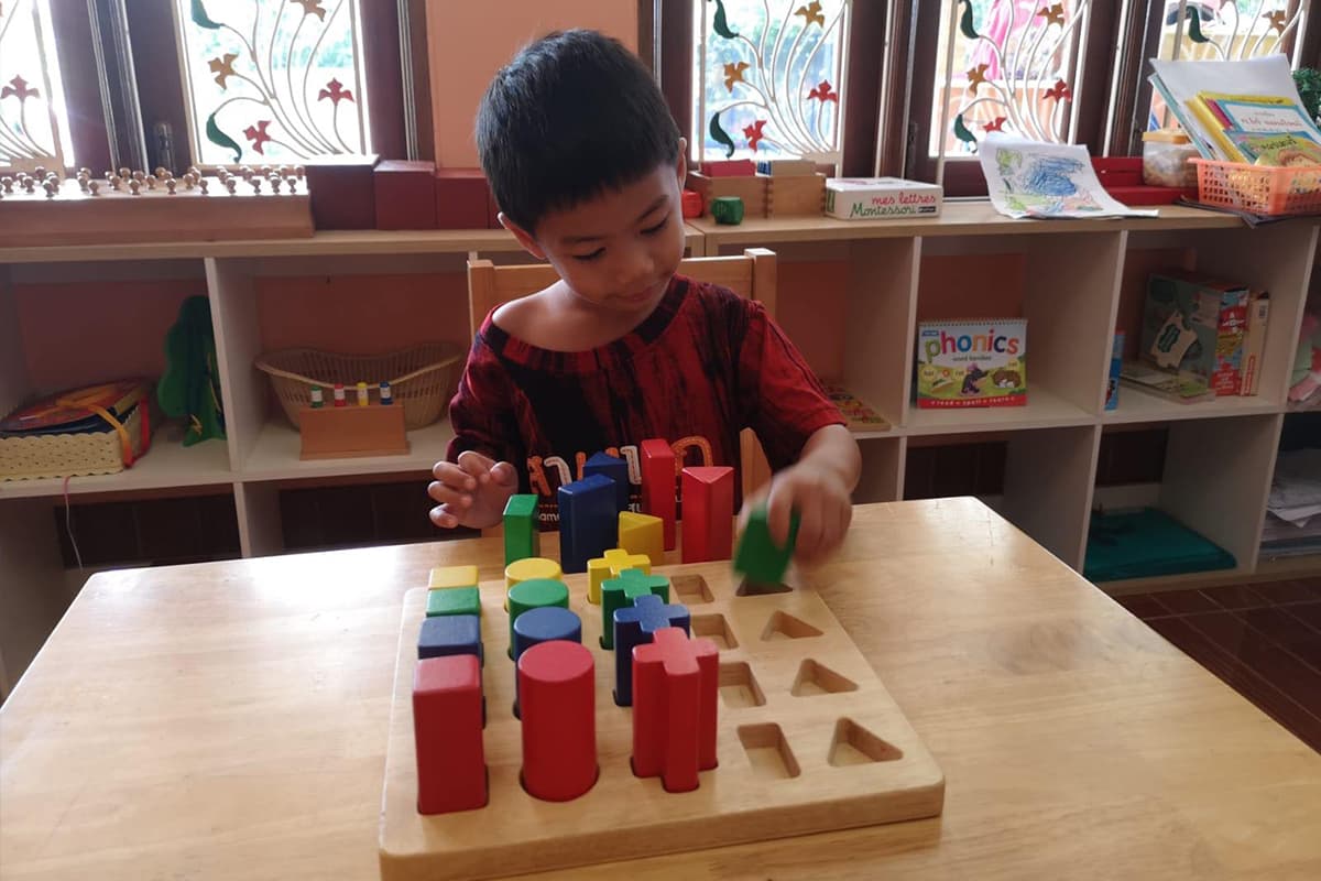 A child fitting coloured cylinders into a wooden Montessori board